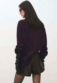 Pulover tricotat de culoare mov închis, design fluid, umeri căzuți, asortat cu pantaloni scurți negri din piele și mănuși lungi negre. Material cu textură netedă.