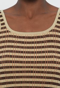 Kudumine tank top ruudukujulise kaelusega. Omab beežit tausta, millel on mustade ja oranžide vahelduvate vertikaalsete triipudega reljeefne soonikujundus.