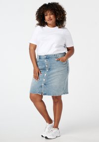 Lichtblauwe denim rok met een sluiting met knopen aan de voorkant en een decoratieve split. Gecombineerd met een wit t-shirt met subtiele hartpatronen. Witte sneakers.