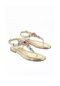 Sandalo dorato con suola piatta e design a T-strap. Decorato con gemme colorate in rosa, blu e viola sulla fascia.