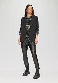Zwarte op maat gemaakte blazer over een zwart-wit gestreepte lange mouwen top, gecombineerd met zwarte leren jogpants en zwarte combatboots.
