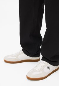 Valged teniskenad, millel on nahkakatted, kummist taldad ja väike logo detail. Kandnud mustade pükstega, rõhutades vaba ja madalat disaini.