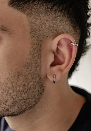 Silberne Creolen schmücken ein kurz geschorenes Ohr und zeigen eine strukturierten, eng geschnittenen Haarschnitt sowie definierten Bart.