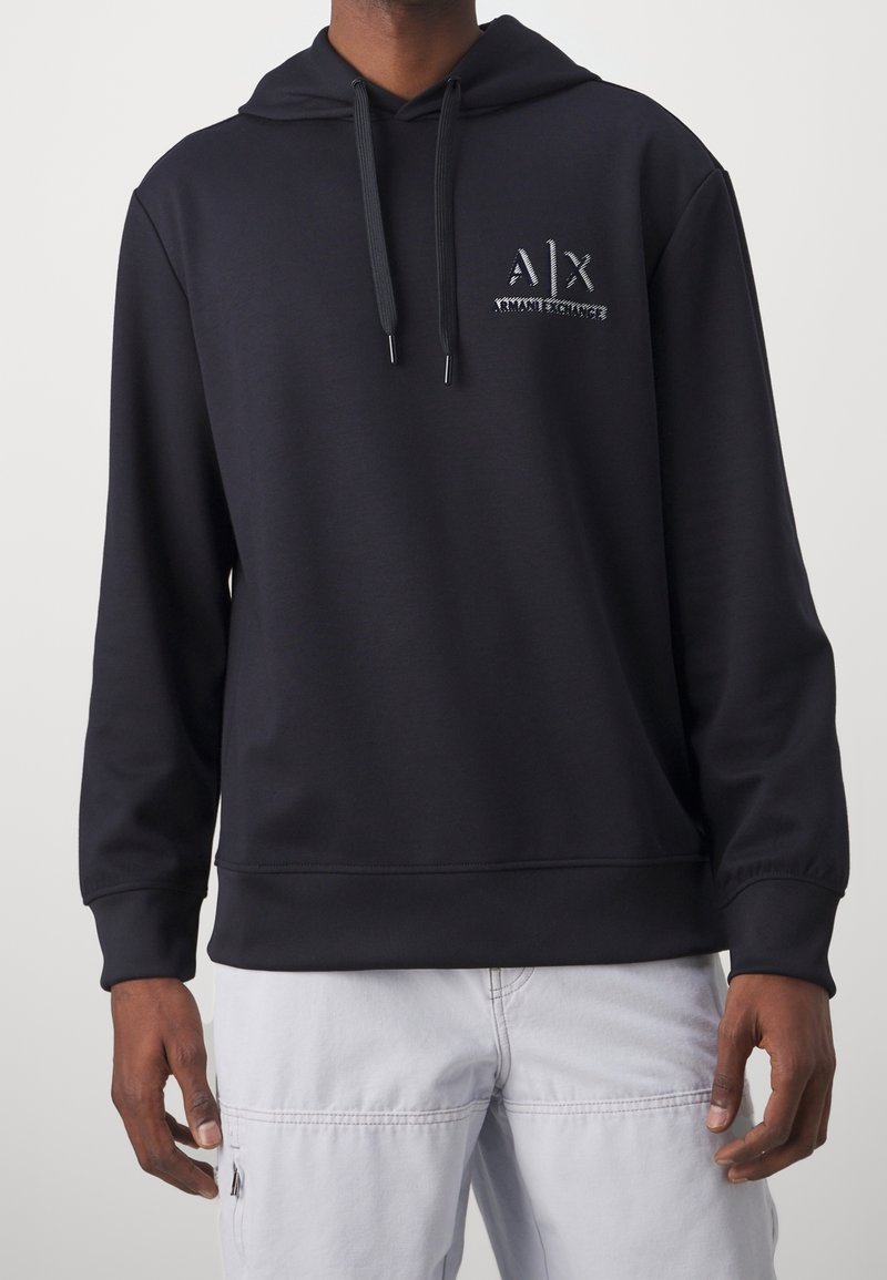 Svart huvtröja med framficka, dragsko i huvan och en texturerad logotyp på bröstet. Tillverkad av mjukt, slätt tyg.