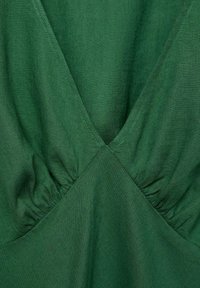Țesătură verde cu un finish moale și texturat. Dispune de un decolteu adânc în formă de V și detalii pliate la bust, creând un aspect ajustat.