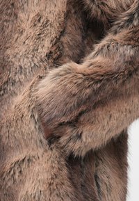 Võltskaevahva kangas pruunides toonides, tiheda ja pehme tekstuuriga, juuste pikkus varieerub, luues rikkaliku ja mitmekihilise välimuse.