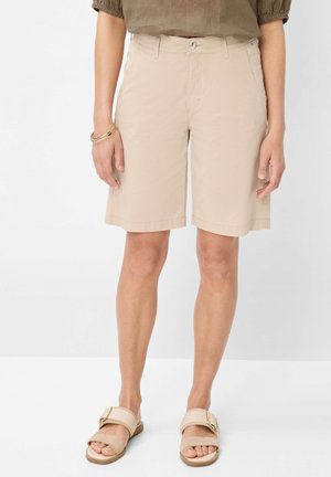 Shorts beiges à mi-cuisses avec une texture lisse, poches avant et fermeture à bouton. Associés à des sandales à glisser légères beiges.