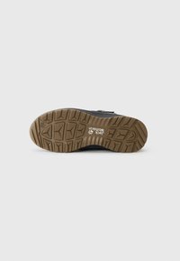 Black shoe with a textured brown rubber outsole, featuring a tread pattern for grip and a logo imprint. No visible laces or hardware.