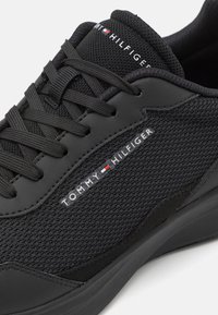 Baskets noires Tommy Hilfiger avec des détails en mesh et cuir, des lacets noirs et le nom de la marque imprimé sur le côté et la languette.