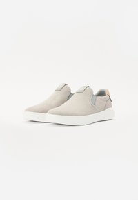 Grå slip-on sko laget av semsket skinn og syntetisk materiale. Har en hvit såle, rund tå, og et lite logo-patch på tungen.
