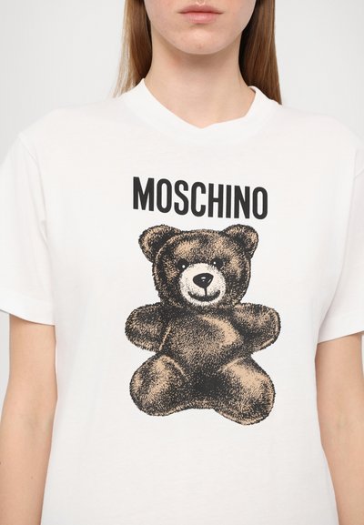 Hvit bomulls t-skjorte med korte ermer, med et svart bjørnegraphikk og "MOSCHINO" tekst over i fet svart skrift.