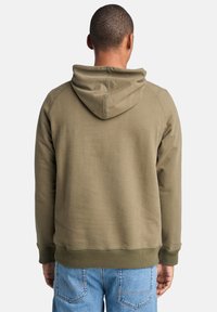 Olijfgroene hoodie met een trekkoordkap, ribgebreide manchetten en zoom, en een zachte textuur, gedragen met lichtblauwe jeans.