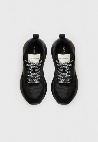 Black athletic shoes with a mesh upper, textured accents, contrasting white laces, and a rounded toe design. Brand label visible inside.