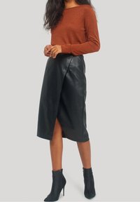 Brun långärmad topp med glans, svart läder midi kjol med en framtill slits, kombinerat med svarta högklackade ankelskor.