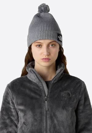 Gray knit beanie with a pom-pom on top, complemented by a soft, gray fleece jacket featuring a zip closure and logo detail.