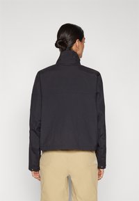 Chaqueta negra con un cuello alto, corte relajado y mangas largas. Fabricada en un tejido suave y ligero, exhibe un diseño minimalista.