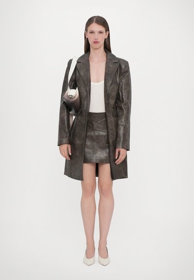 Brown leather coat with a tailored design, paired with a matching mini skirt. White top and shoes complete the look, along with a sleek handbag.