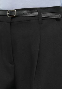 Μαύρο ραμμένο παντελόνι με υφή, διακοσμημένο με μαύρη δερμάτινη ζώνη και ασημί αγκράφα. Ορατές τσέπες στα πλαϊνά.