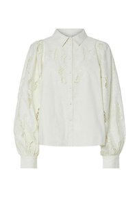 Hvit bluse med knapplukking foran, som har intrikate broderte detaljer og gjennomsiktige blondesolermer. Ermene er puffete med en tettsittende mansjett.