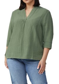 Losse, olijfgroene blouse met v-hals en driekwartmouwen; met een gestructureerde stof met subtiele verticale lijnen.
