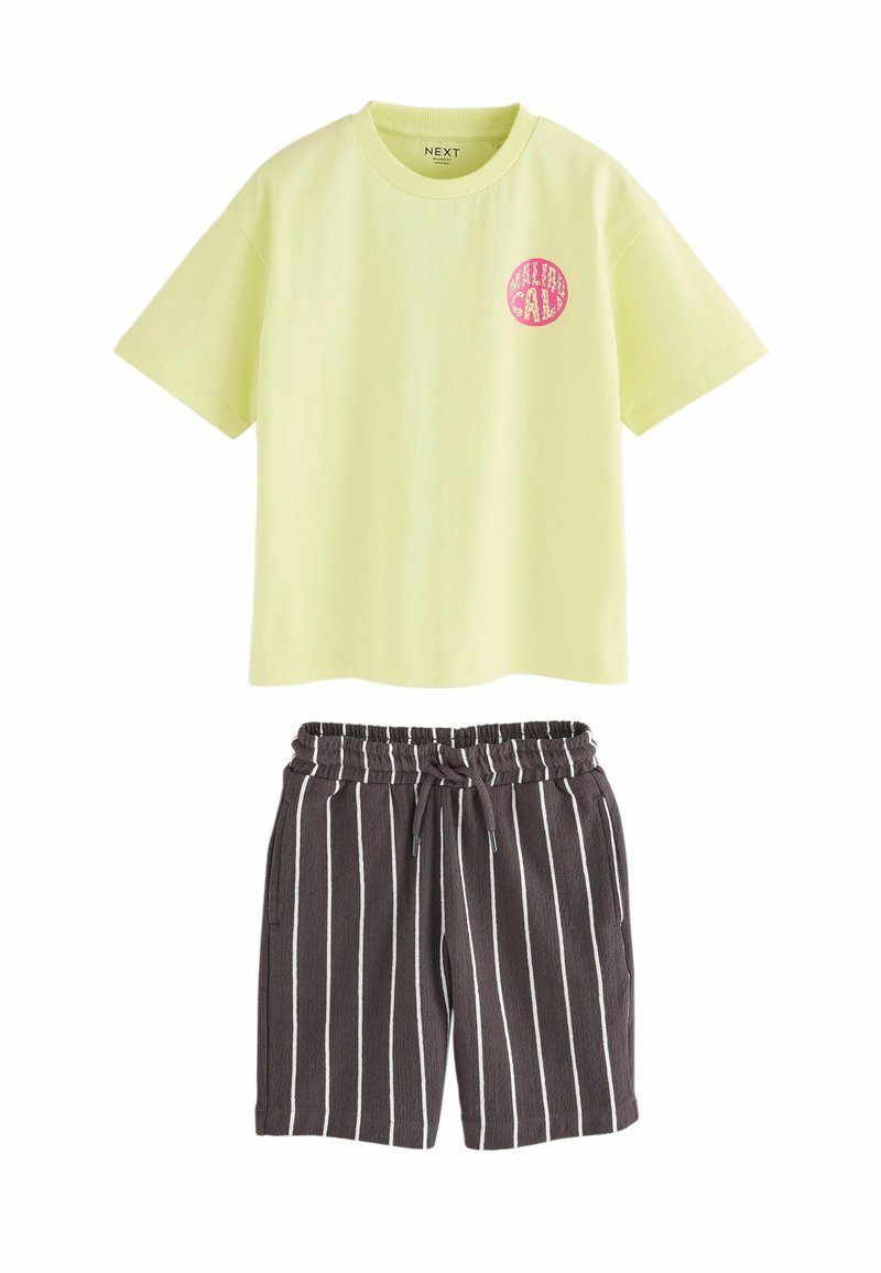Lichtgele T-shirt met korte mouwen en een roze cirkelvormig logo, gecombineerd met donkergrijze shorts met witte verticale strepen en een elastische tailleband.