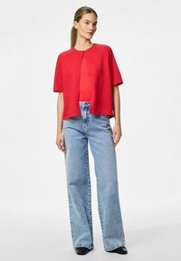 Crvena kratka kardigan s kratkim rukavima i zatvaranjem na gumbe, uparen sa svijetloplavim širokim trapericama visokog struka. Glatka tekstura i ležeran kroj.