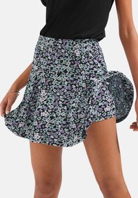 Cvjetna suknja s crnom pozadinom, koja sadrži mala mente zelena i ljubičasta cvijeća. Elastični pojas, lepršavi dizajn dužine do sredine bedra.