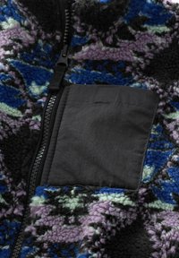Veste en polaire avec un motif bleu, noir et violet, fermeture éclair noire et une poche carrée noire unie sur la poitrine.
