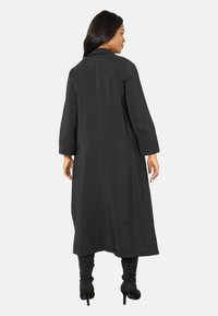 Schwarzer langer Mantel mit lockerem Schnitt, kragen und Dreiviertelärmeln. Hergestellt aus leichtem Material mit glatter Textur.