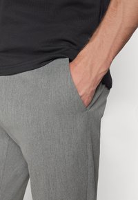 Gray tailored pants with a fine texture and side pockets, worn with a dark shirt, hand resting on the pant pocket.