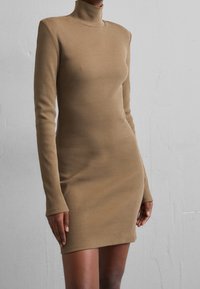 Ribbede, tæt siddende kjole i en tan farve med lange ærmer og en høj, tætsiddende halsudskæring. Glat tekstur og kort fald.