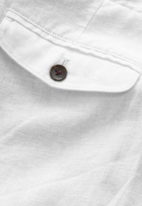 Tissu en lin blanc avec une finition texturée, comportant un col de chemise et un bouton rond marron foncé avec un trou central.