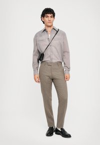 Pruhovaná košile na knoflíky v šedých tónech, spárovaná s hnědými texturovanými kalhotami. Doplněno malou černou kabelkou přes rameno a černými botami.