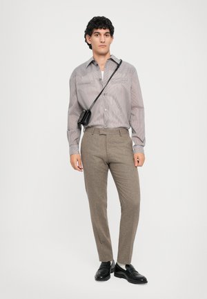 Ριγέ πουκάμισο σε γκρι τόνους, συνδυασμένο με καφέ υφασμάτινο παντελόνι. Τα αξεσουάρ περιλαμβάνουν μια μικρή μαύρη τσάντα ώμου και μαύρα παπούτσια.