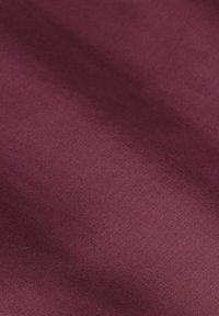 Glad bordeaux satijnstof met zachte plooien die subtiele lichtreflecties en zachte schaduwen over het oppervlak creëren.