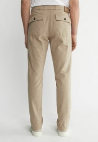 Beige Twill-Hosen haben einen geraden Schnitt, zwei Gesäßtaschen mit Knopfverschlüssen und ein Kunstlederlabel am Bund.