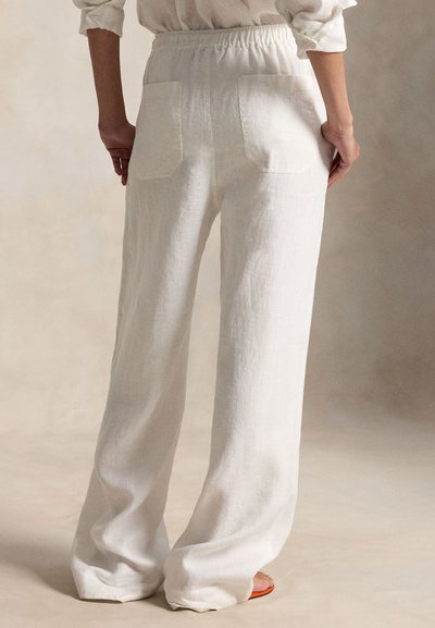 Άτομο που φοράει άνετο, λινό παντελόνι με ψηλή μέση και πίσω τσέπες, όντας ξυπόλητο μπροστά σε ουδέτερο φόντο.