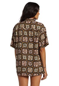 Short-sleeve, oversized shirt features a black background with colorful floral and leaf patterns in squares, made from lightweight fabric.