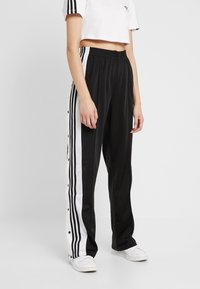 Svarta träningsoverallbyxor med vita sidosträck och snap-knappsstängning. Tillverkade av glatt tyg, med elastisk midja och avslappnad passform.