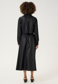 Melnas mākslīgās ādas kleita ar īsu topu, garām piedurknēm, elastīgu jostu un plūstošu svārku, ar pogāmiem piedurkņu galiem un gludu tekstūru.