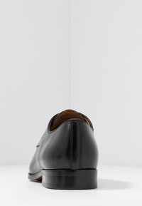 Chaussure habillée en cuir noir vue de l'arrière, mettant en valeur la finition lisse et les détails de couture sur le talon et la semelle.