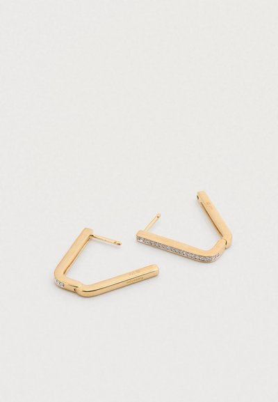 Χρυσά γεωμετρικά σκουλαρίκια με τετράγωνο σχέδιο που διαθέτει μια σειρά μικρών διαφανών στρας κατά μήκος μιας ακμής. Κατασκευασμένα από μέταλλο με γυαλιστερό φινίρισμα.