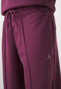 Viininpunaiset collegehousut, joissa on joustava vyötärönauha ja kiristysnauha. Vasemmassa reisessä pieni hopeinen Jumpman-logo. Sileä puuvillakangas.