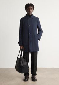 Jūras spēku krāsas, vidēja garuma mēteli ar pogu priekšpusi, lielu apkakli un sānu kabatām, nēsā virs melnā tērpa un saskaņots ar melnām biksēm un somu.