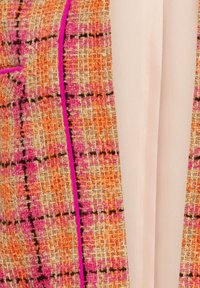Veste tissée avec un motif à carreaux orange, rose et beige. Caractérisée par un design élégant, un tissu texturé et un bord contrastant rose le long des contours.