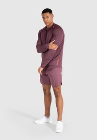 Mörkröd långärmad träningsskjorta och matchande shorts, med en subtil textur och sidoklykor. Vita sneakers med logotypdetalj.