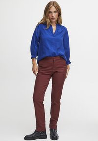 Blå, löst sittande blus med långa, draperade ärmar; ihop med åtsittande, vinröda byxor och svarta ankelstövlar med kraftiga sulor och metalldetaljer.
