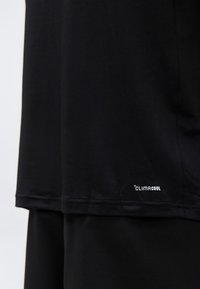 Gros plan sur un tissu de sport ClimaCool noir montrant un textile respirant avec un petit logo ClimaCool blanc près de l'ourlet.