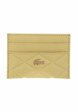 Petit porte-cartes beige avec une texture matelassée, deux emplacements pour cartes, et un petit logo métallique de crocodile centré à l'avant.