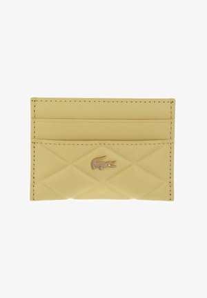 Petit porte-cartes beige avec une texture matelassée, deux emplacements pour cartes, et un petit logo métallique de crocodile centré à l'avant.